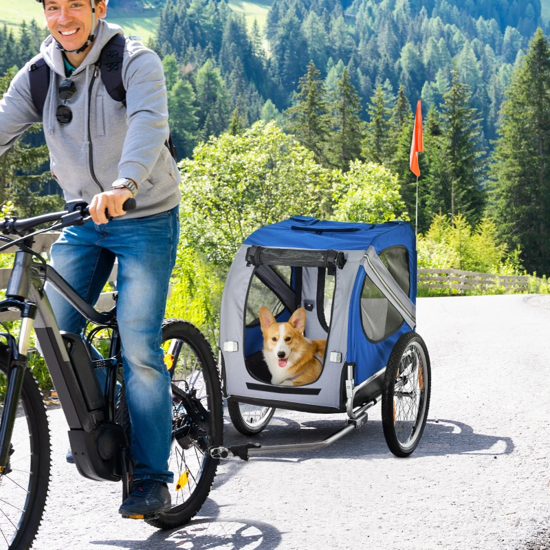 cyclist towing corgi in blue bike trailer on mountain road.