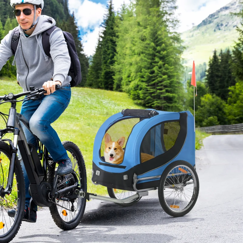 corgi riding in blue bike trailer attached to bicycle on mountain road.