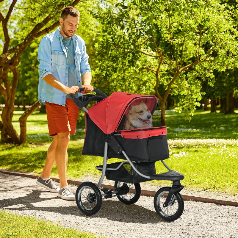 man pushing corgi in red stroller on sunny park trail.