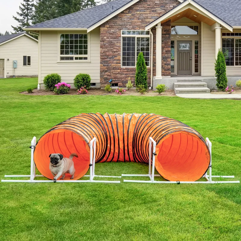 Dog exiting bright orange agility tunnel on open lawn.