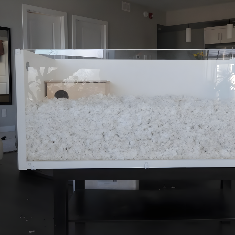 Deep-bedding hamster cage with a wooden multi-chamber hideout partially covered.