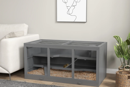 Large grey hamster cage setup beside sofa in living room.