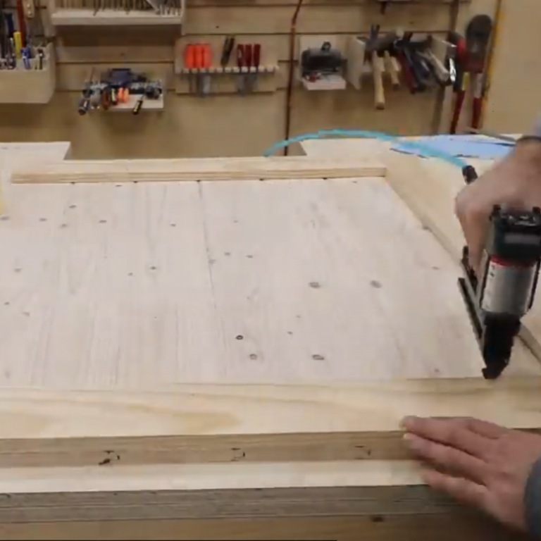 Framing the wooden dog gate panel with trim boards during construction in a workshop.