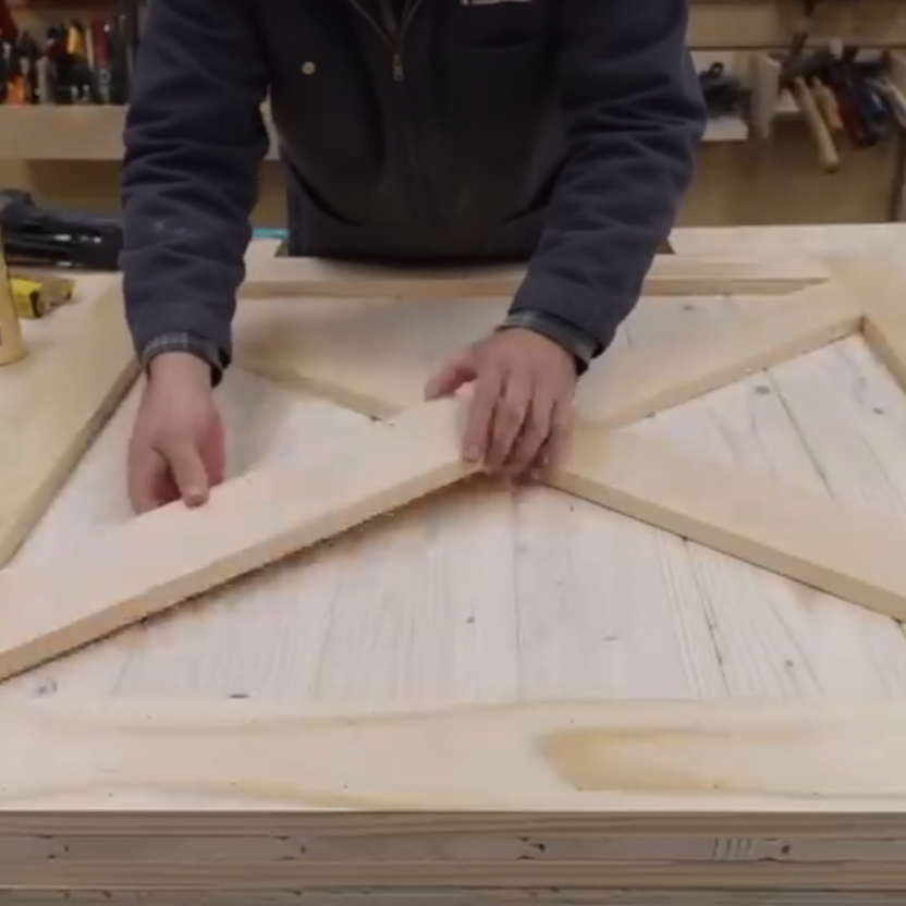 Positioning cross-brace trim pieces to form the X pattern on a wooden dog gate.