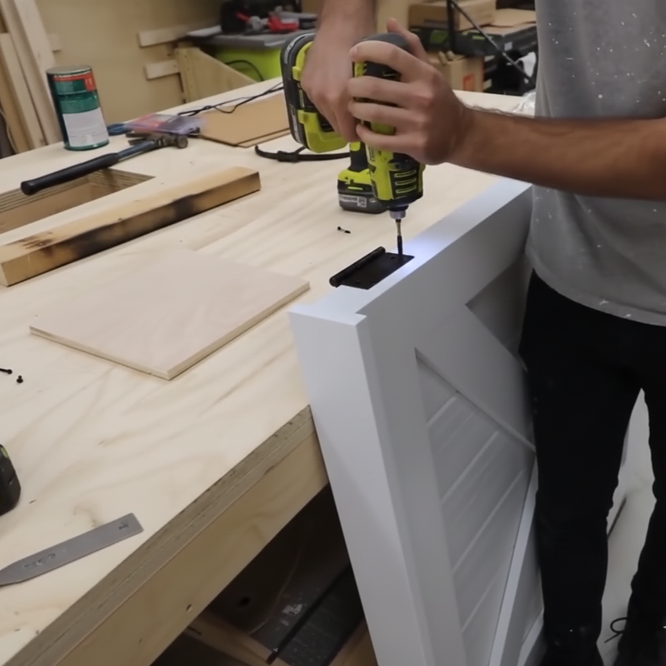Attaching a white wooden dog gate to a wall opening in a hallway during installation.