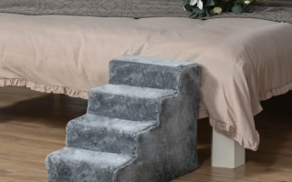 Soft grey foam dog stairs placed beside a bed for easy pet access.