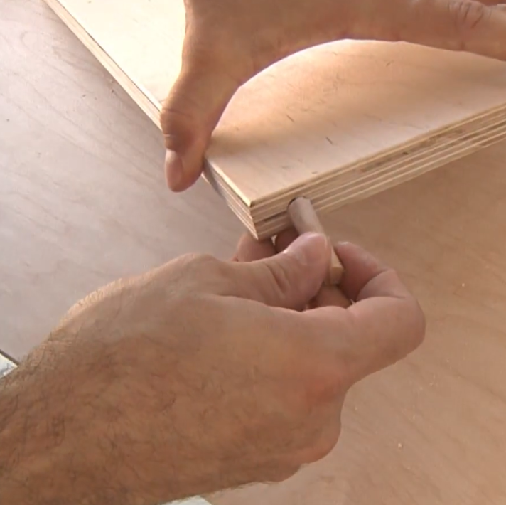 Hands inserting a wooden dowel into a plywood edge during dog stair assembly.