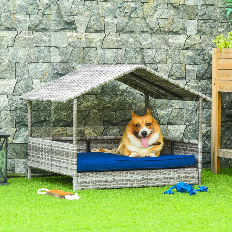 Happy corgi rests on a blue cushion in a covered outdoor wicker dog bed.